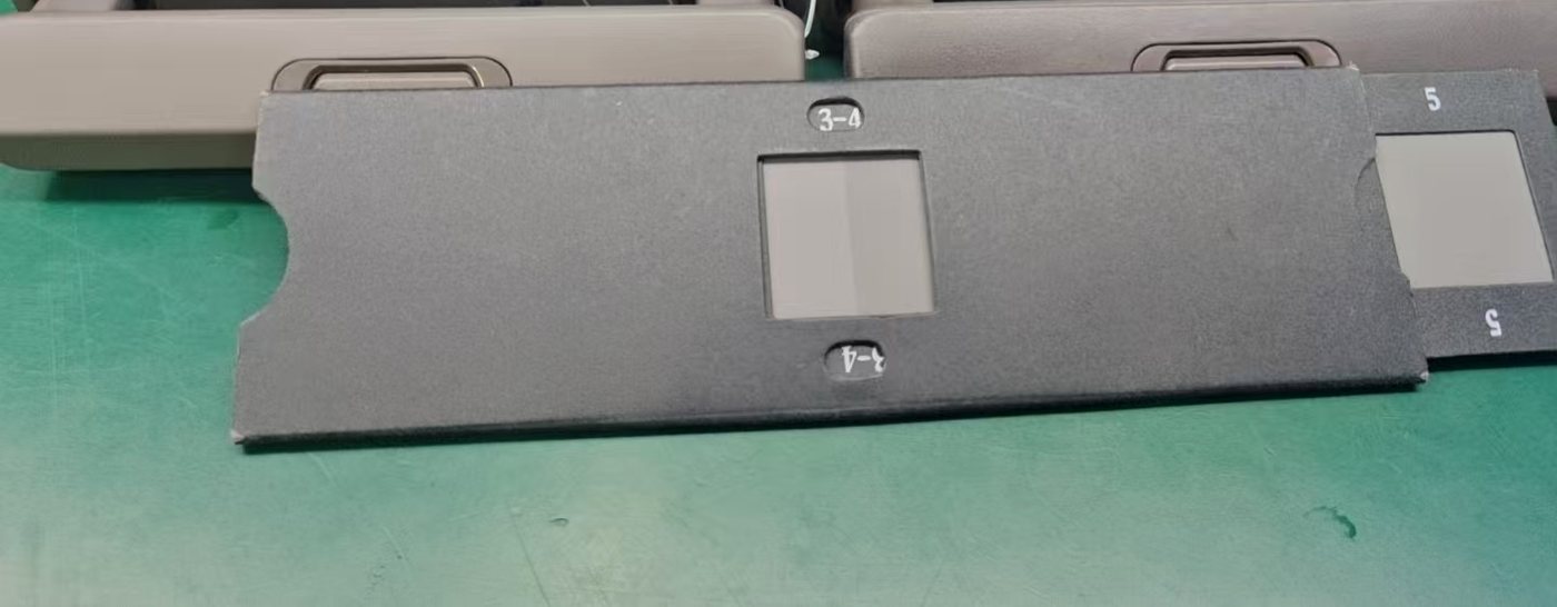 A grey scale card resting on a workbench against grey trolley handle mouldings, with the grade 3-4 and 4-5 reference pairs visible on the card