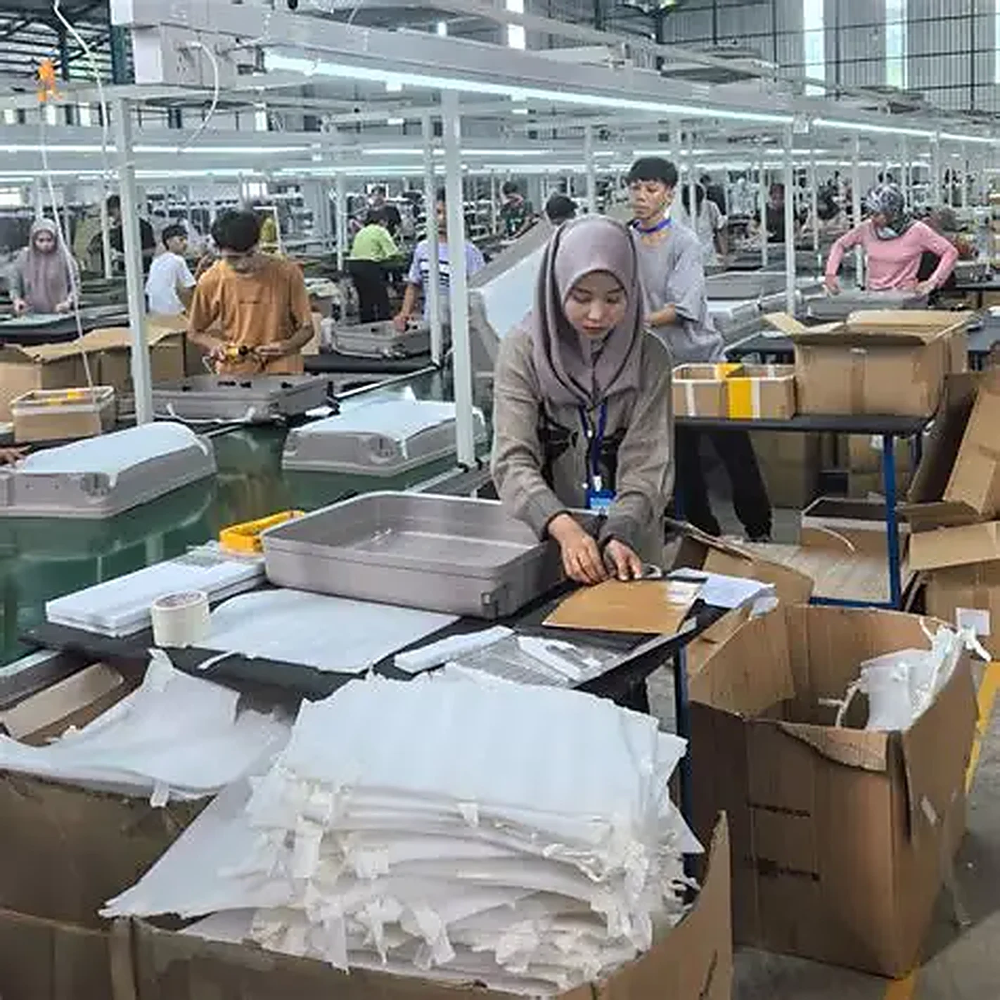 Workers assembling hardside PC shells at their stations, working documents on the bench
